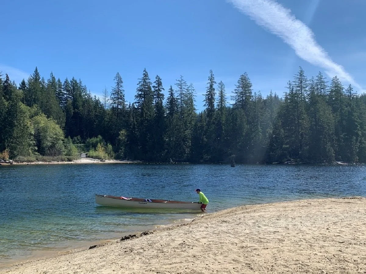 A boy holding a floating canoe at a lakes edge.