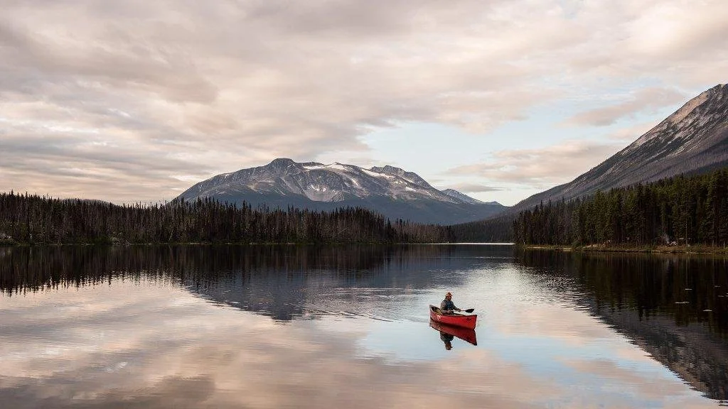 A solo canoe paddler on a lake with mountains behind