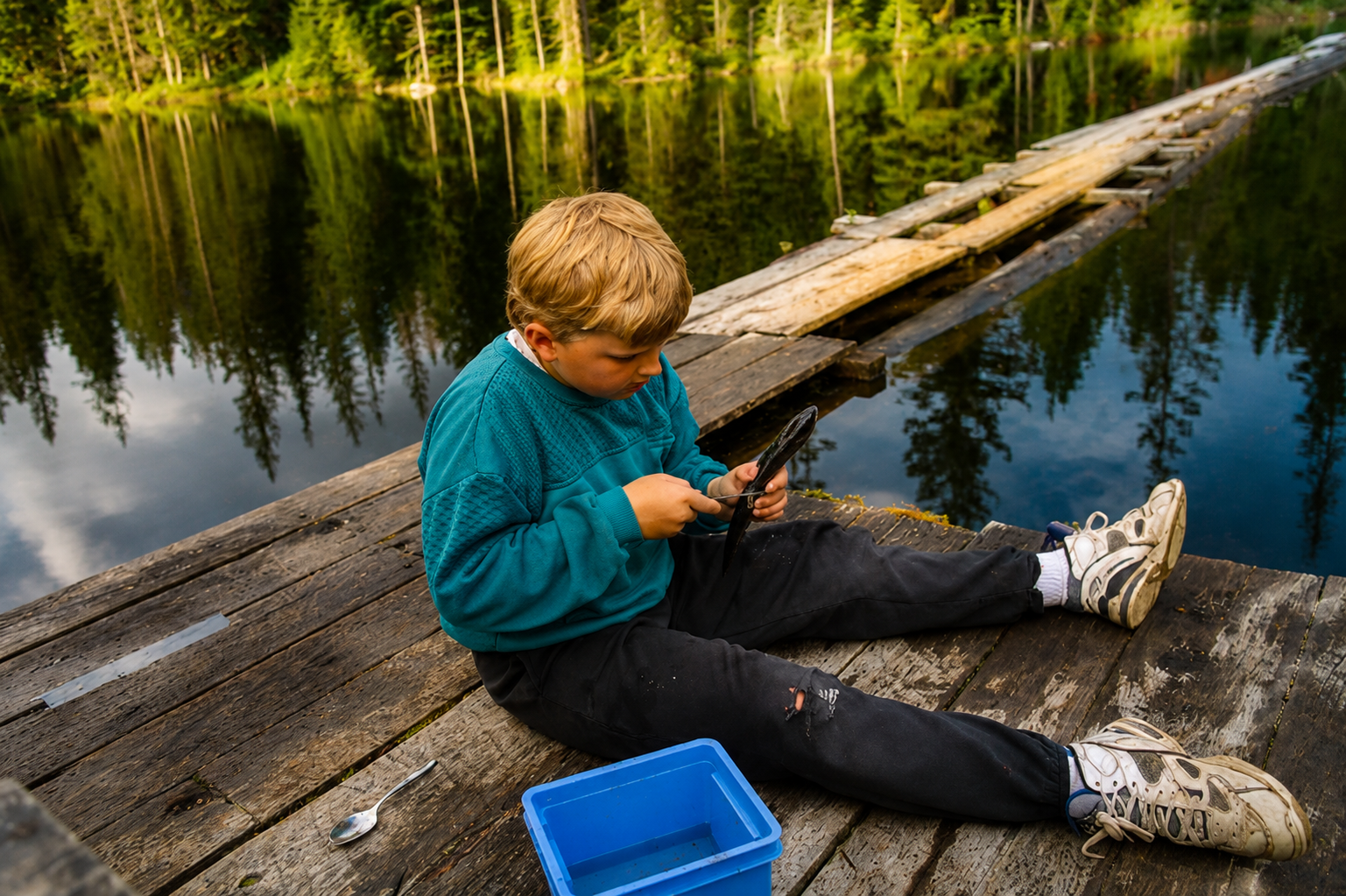 A young boy cleaning a lake fish on a floating dock