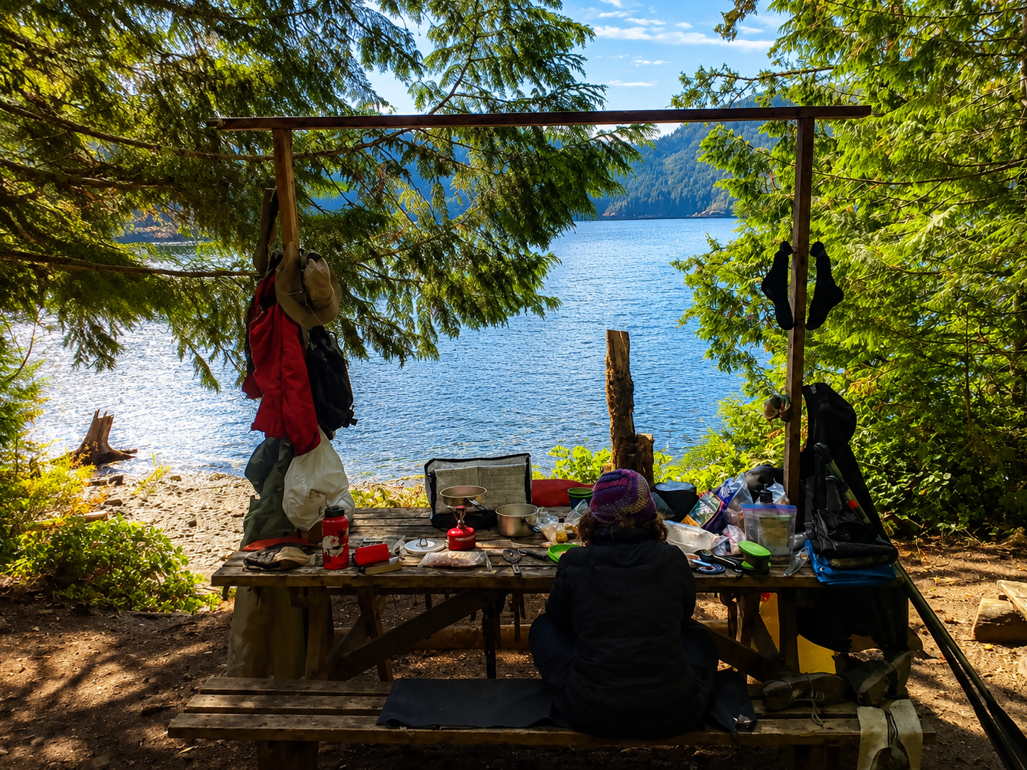 Camping gear spread out over a picnic table at camp, on the lake's edge.