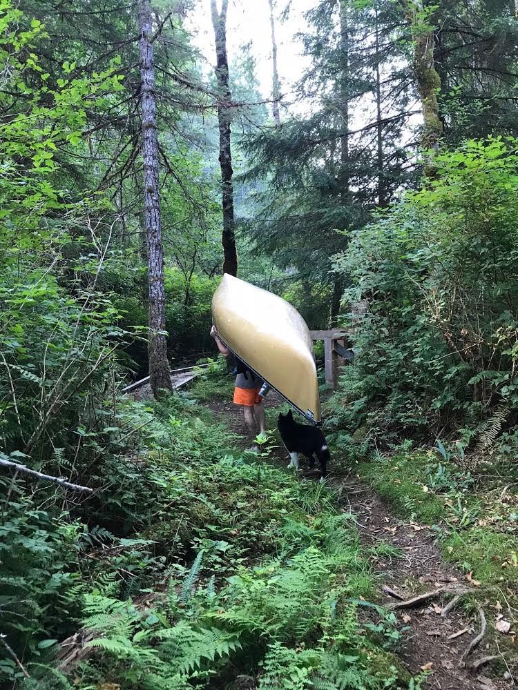 A man portaging an ultralight canoe on a trail with his dog