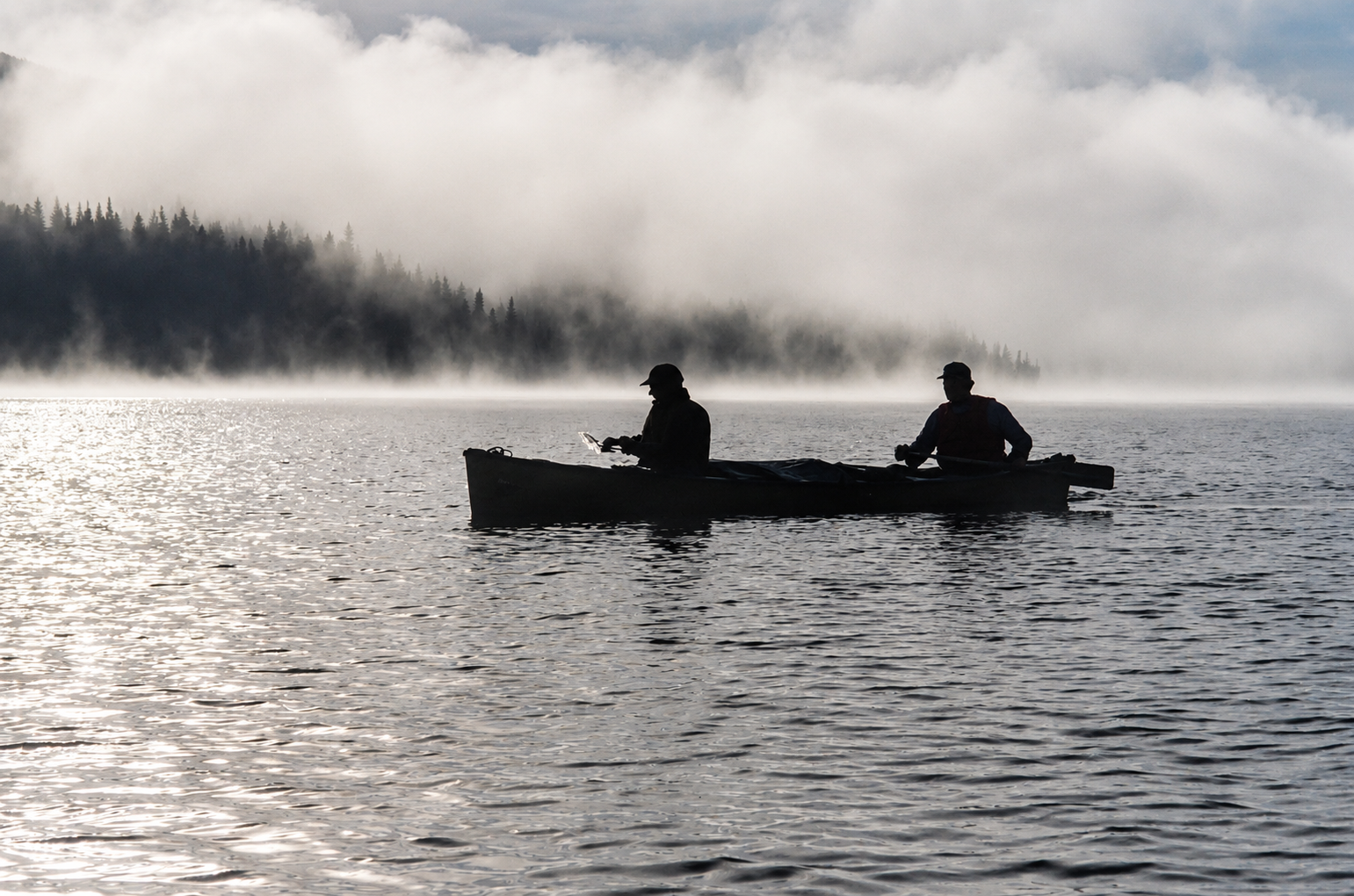 Two men paddling a canoe on a misty morning lake