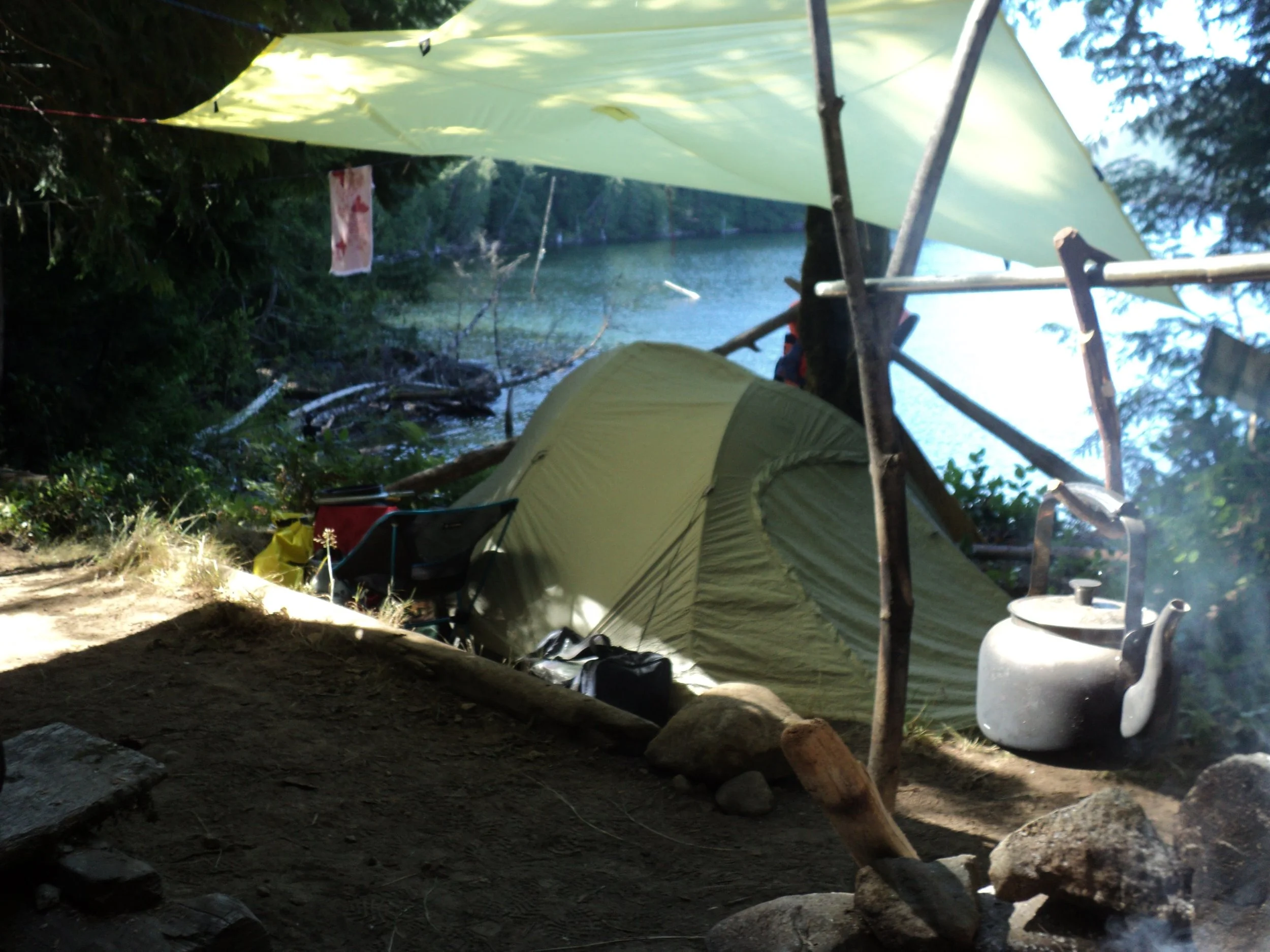 A tent pitched under a tarp on a lake
