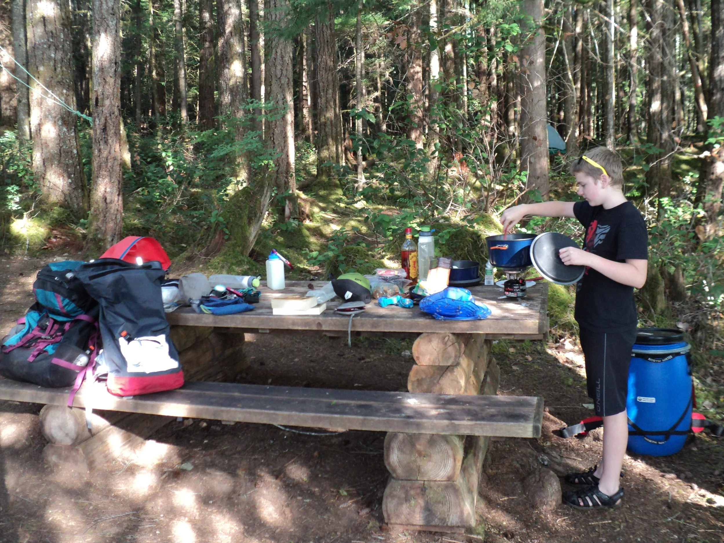A teenage cooking camp dinner at picnic table