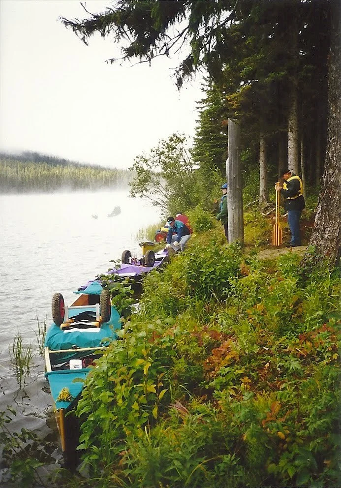 Three canoes at rest on the edge of the lake with wheel carts sitting on the gear.