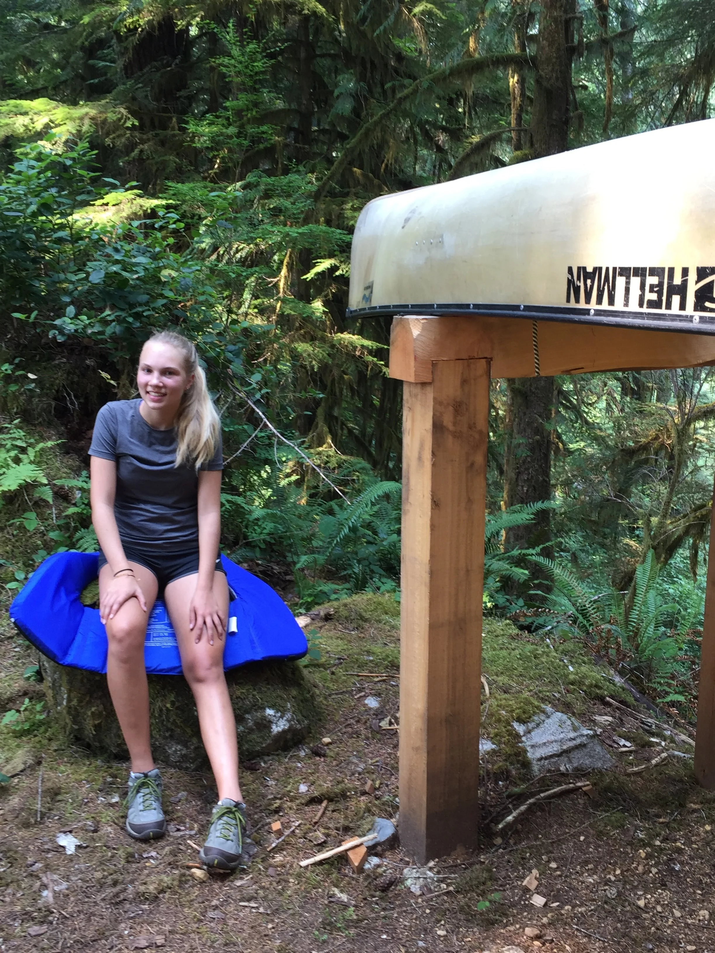 A girl resting on trails edge next to a canoe
