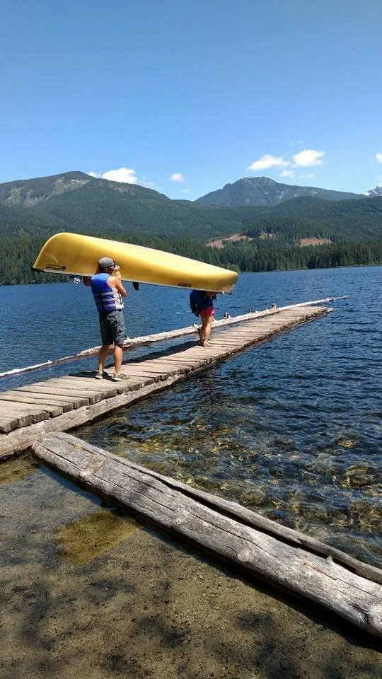 Two people carrying a canoe on a lake dock