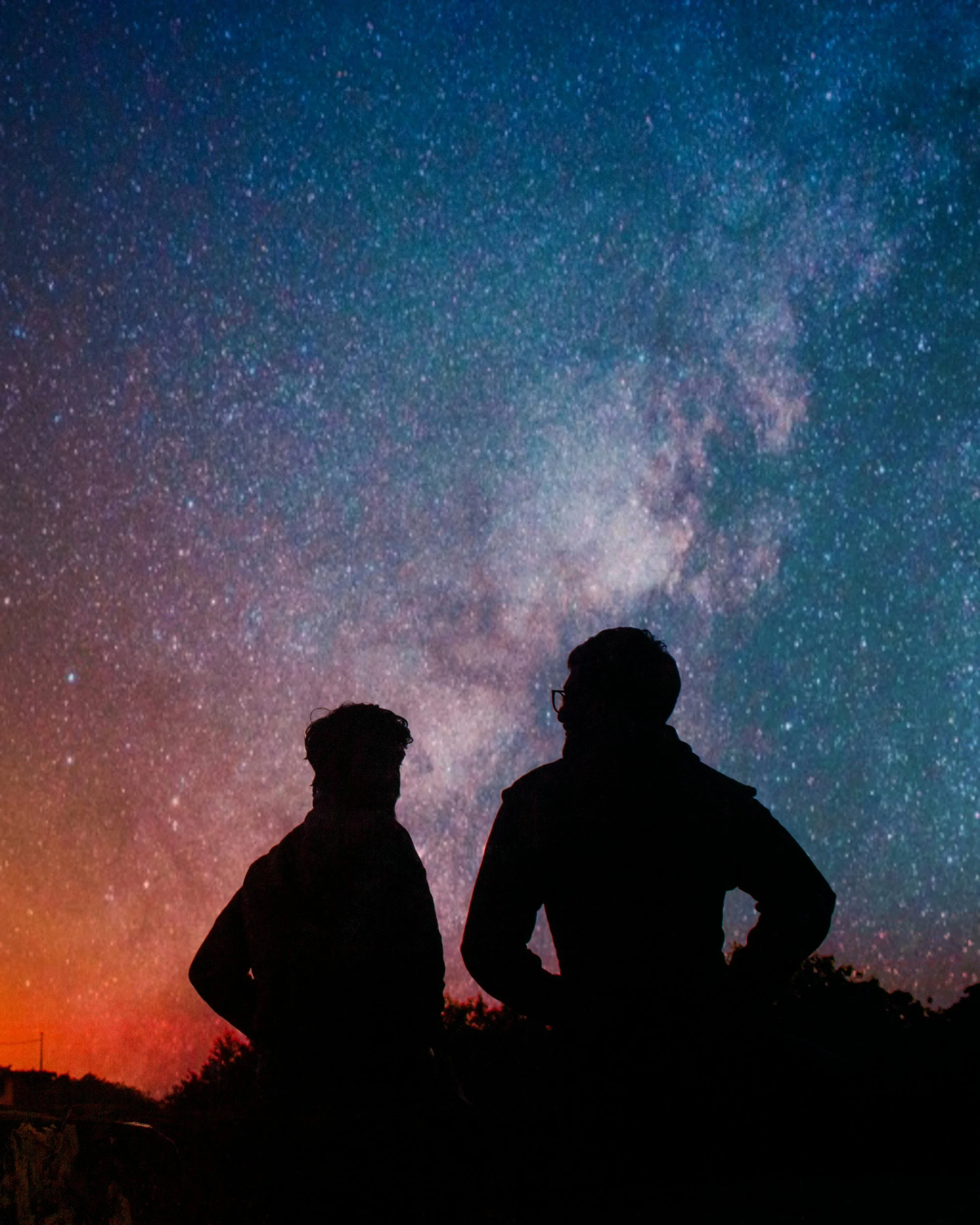 Silhouettes of two people sitting and conversing against a vibrant, starry night sky with the Milky Way galaxy visible.