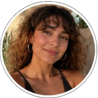 A young woman with curly hair and hoop earrings smiling at the camera