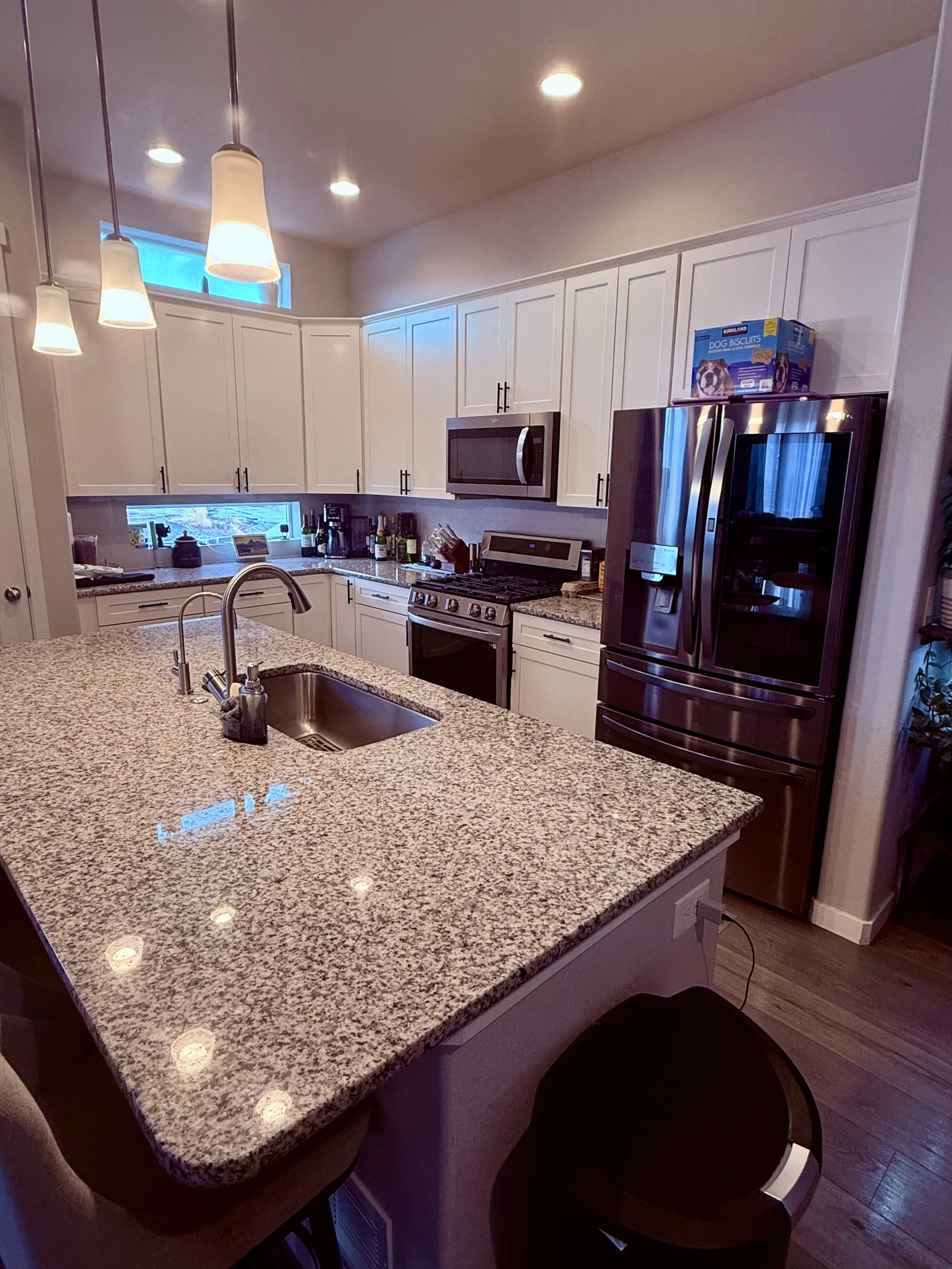 Modern kitchen with granite countertop island, stainless steel refrigerator, microwave, stove, pendant and recessed lighting.