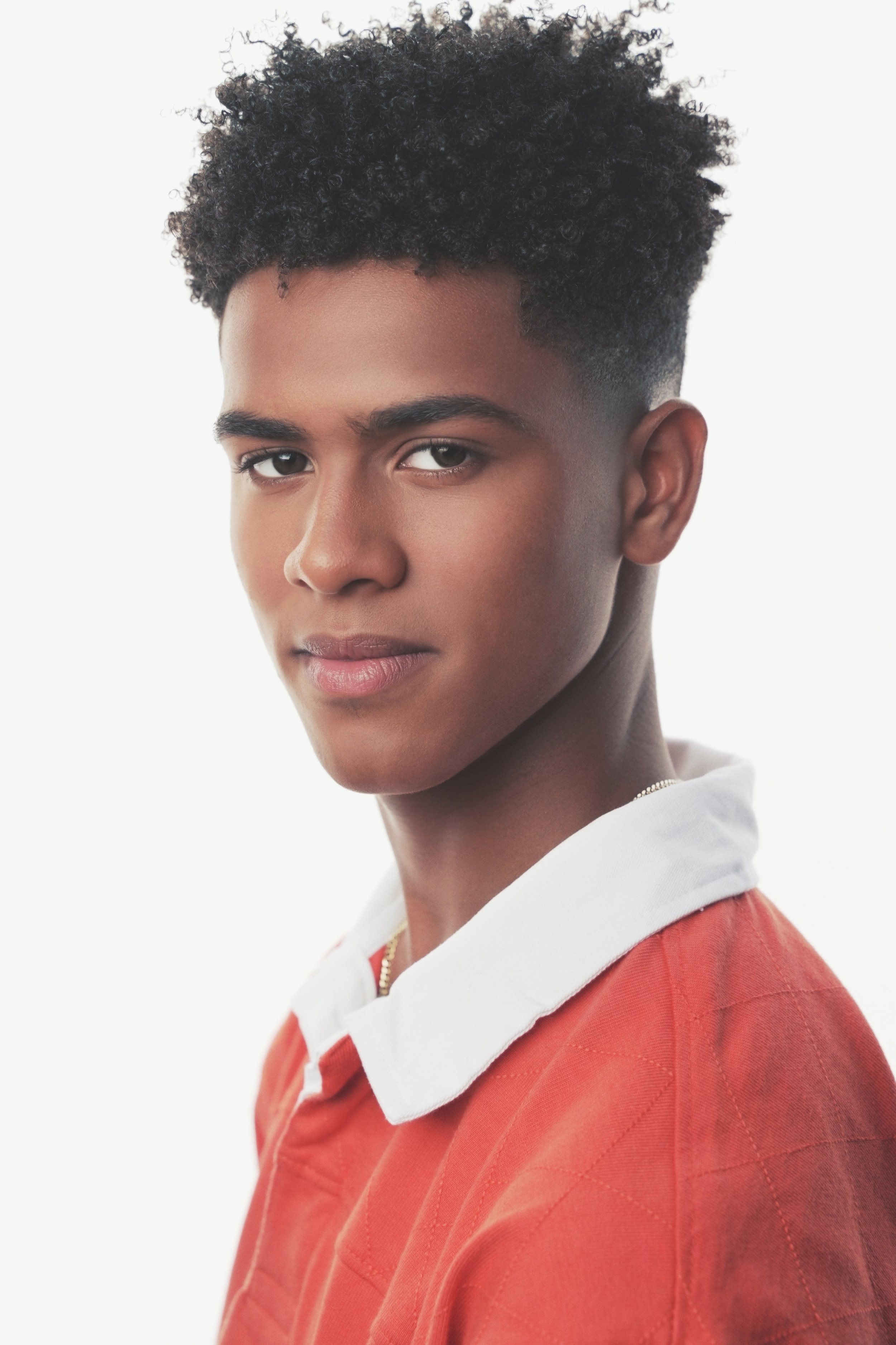 Young man with curly hair wearing a red shirt with a white collar, looking at the camera.