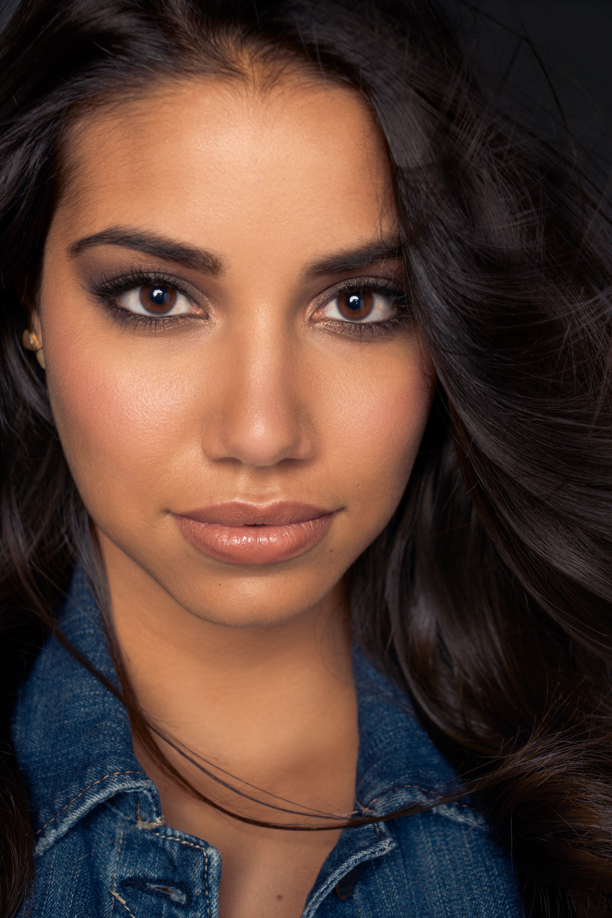 Portrait of a woman with dark hair and makeup, wearing a denim jacket.