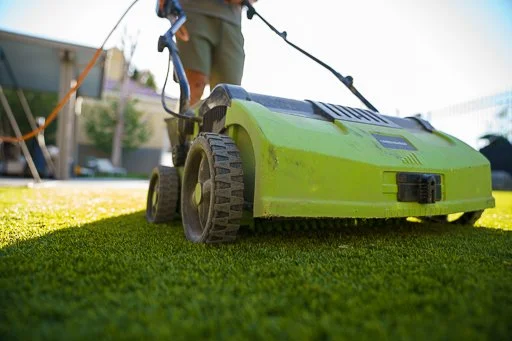 Person using a green lawnmower to cut grass in a yard.