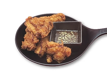 Fried chicken pieces on a black plate with a small square dish of sauce containing sesame seeds.