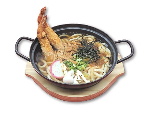 Udon noodle soup with tempura shrimp and assorted toppings in a black bowl on a wooden board.