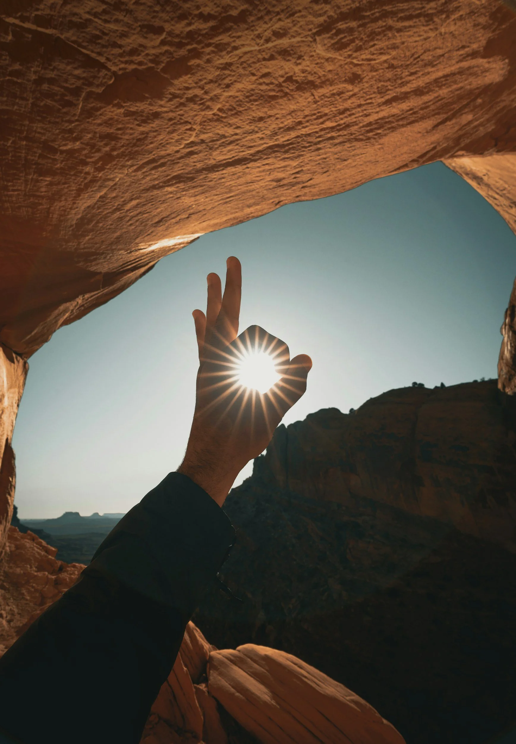 Hand help up to sky sun shining through ok hand sign. Mountain high desert setting.