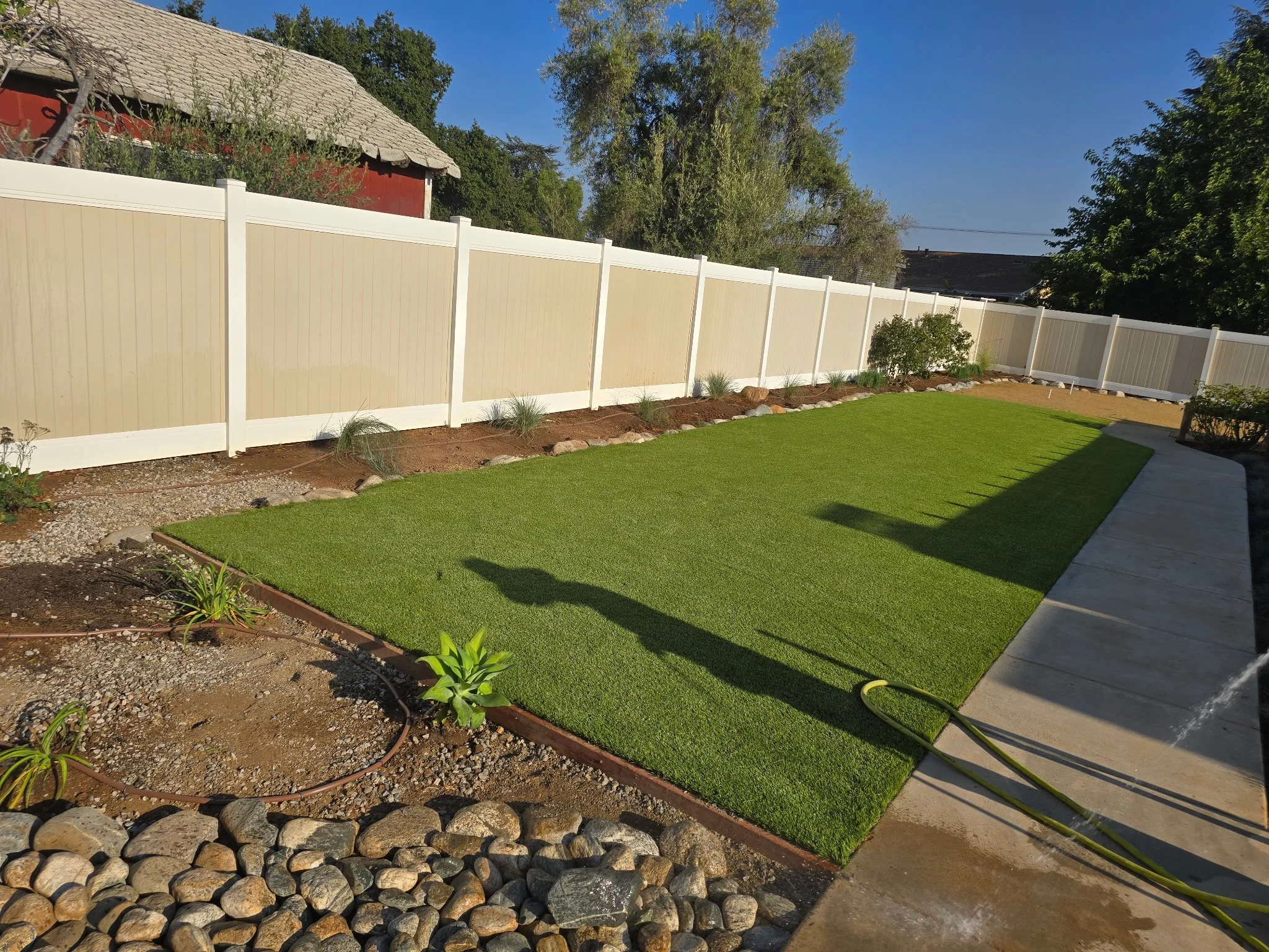 LANDSCAPING & LIGHTING | Artificial turf bordered by planting beds, decorative rock, and a concrete walkway.