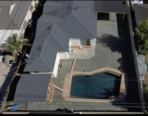 Aerial view of a backyard pool and concrete patio beside a house.
