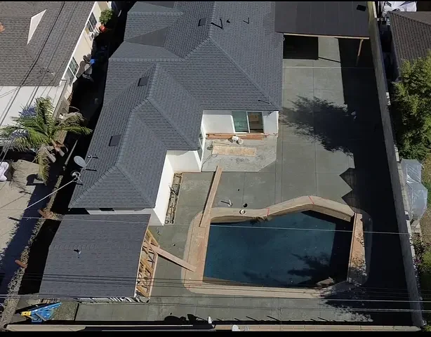 Aerial view of a backyard swimming pool, concrete patio, and surrounding walls.
