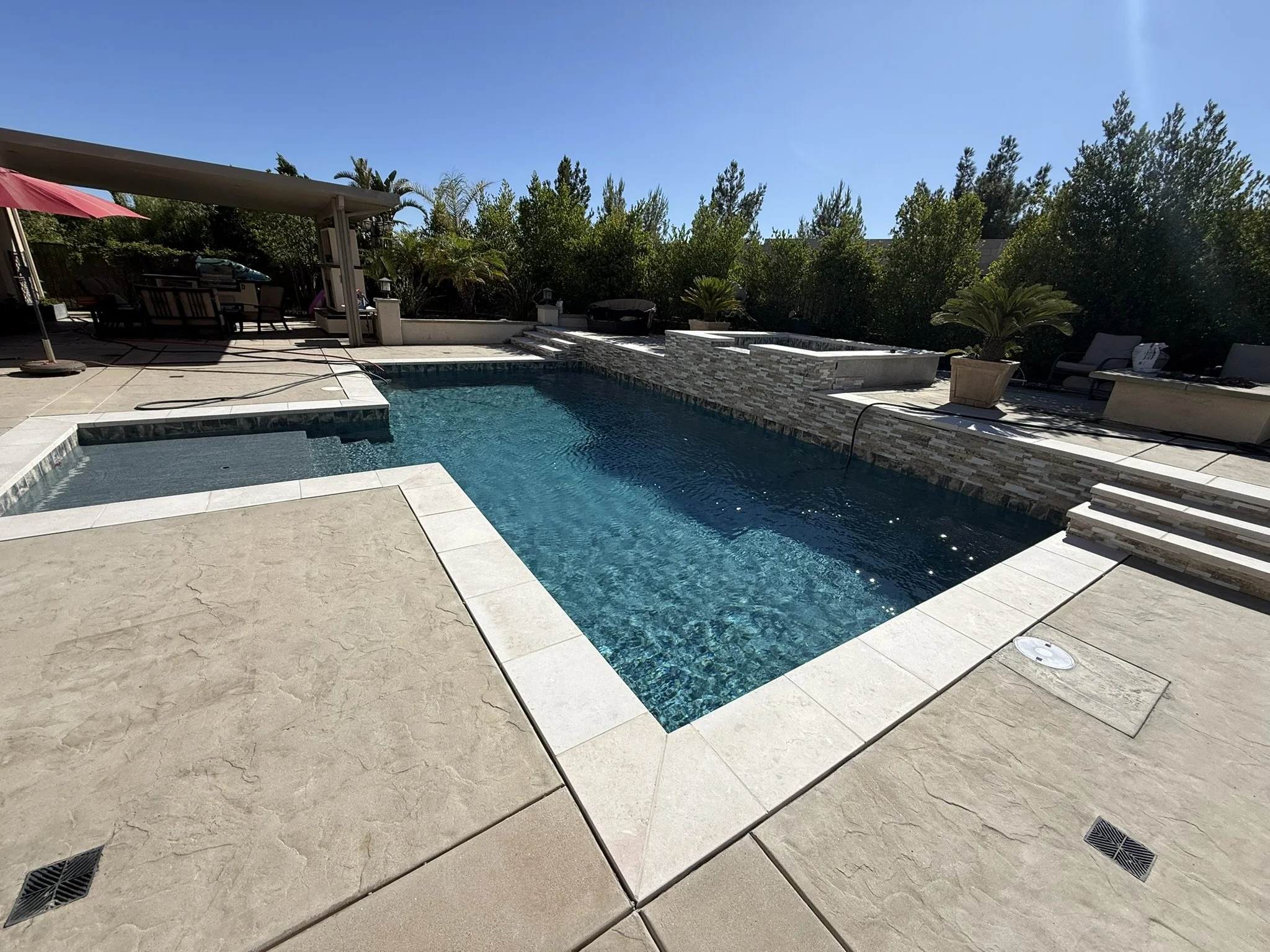 POOLS & POOLSIDE PATIOS | Pool and spa with stone-faced walls, broad coping, and a surrounding patio.