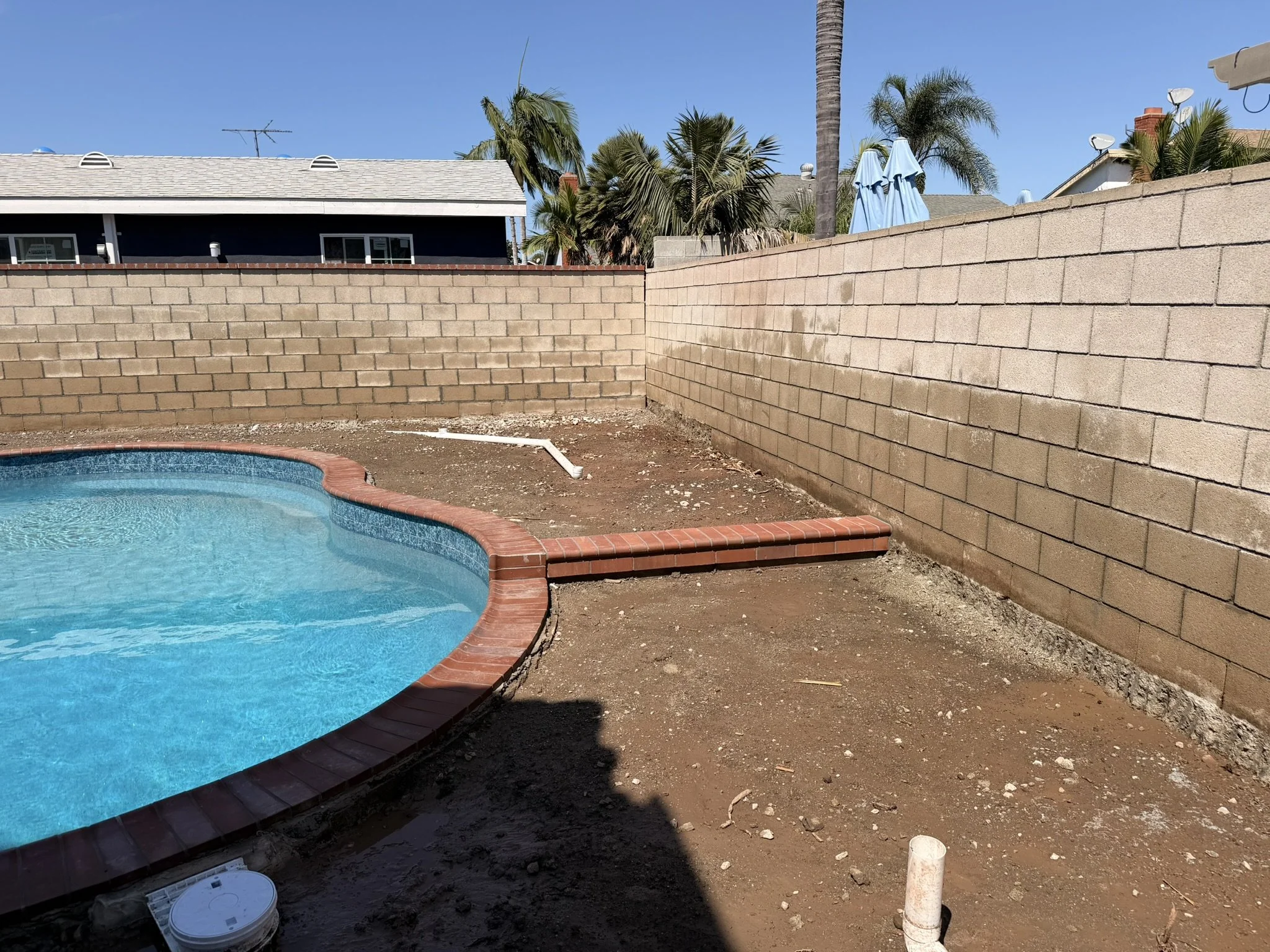 POOLS & POOLSIDE PATIOS | Before — existing pool with bare soil around the perimeter, before the patio work.