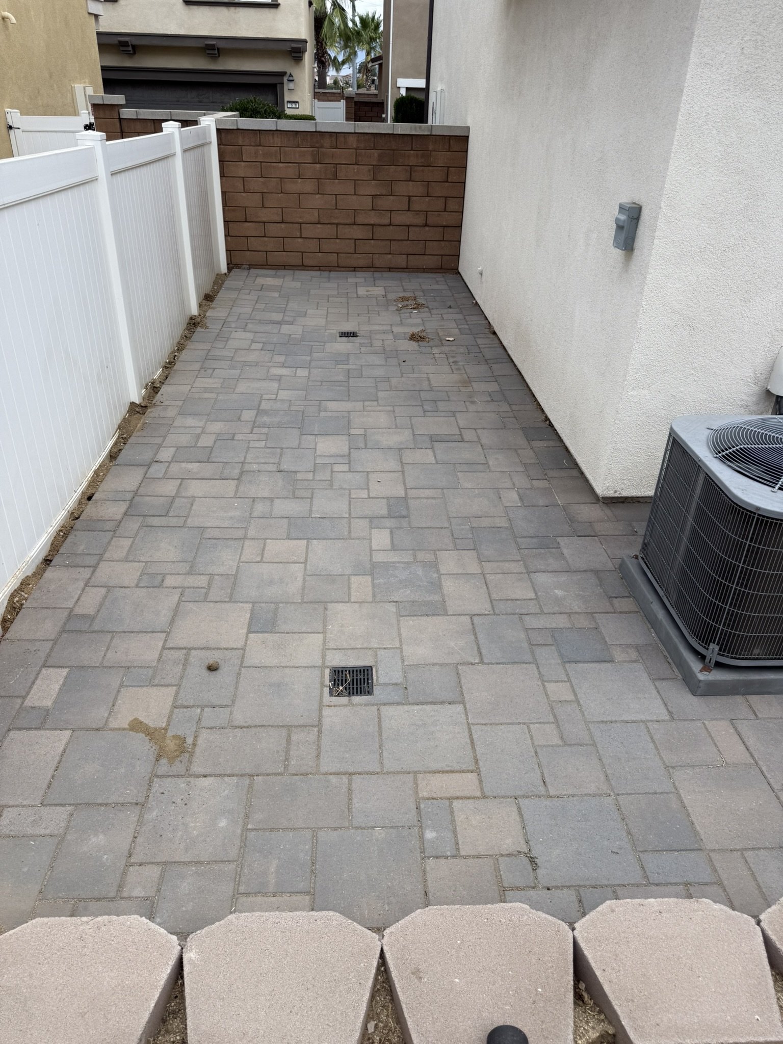 PAVERS & OUTDOOR LIVING | Interlocking paver walkway with inset drainage grates beside the home.
