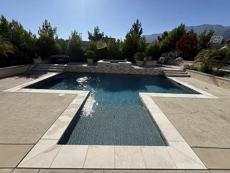 Swimming pool and raised spa with stone coping and surrounding patio.