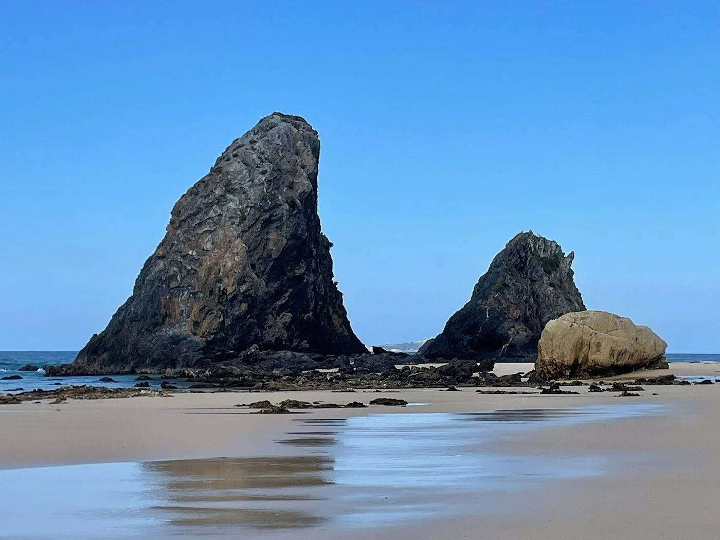 Large rocks and boulders scattered across a sandy beach, with the ocean gently meeting the shore under a clear blue sky, an iconic and serene coastal scene in Narooma.
