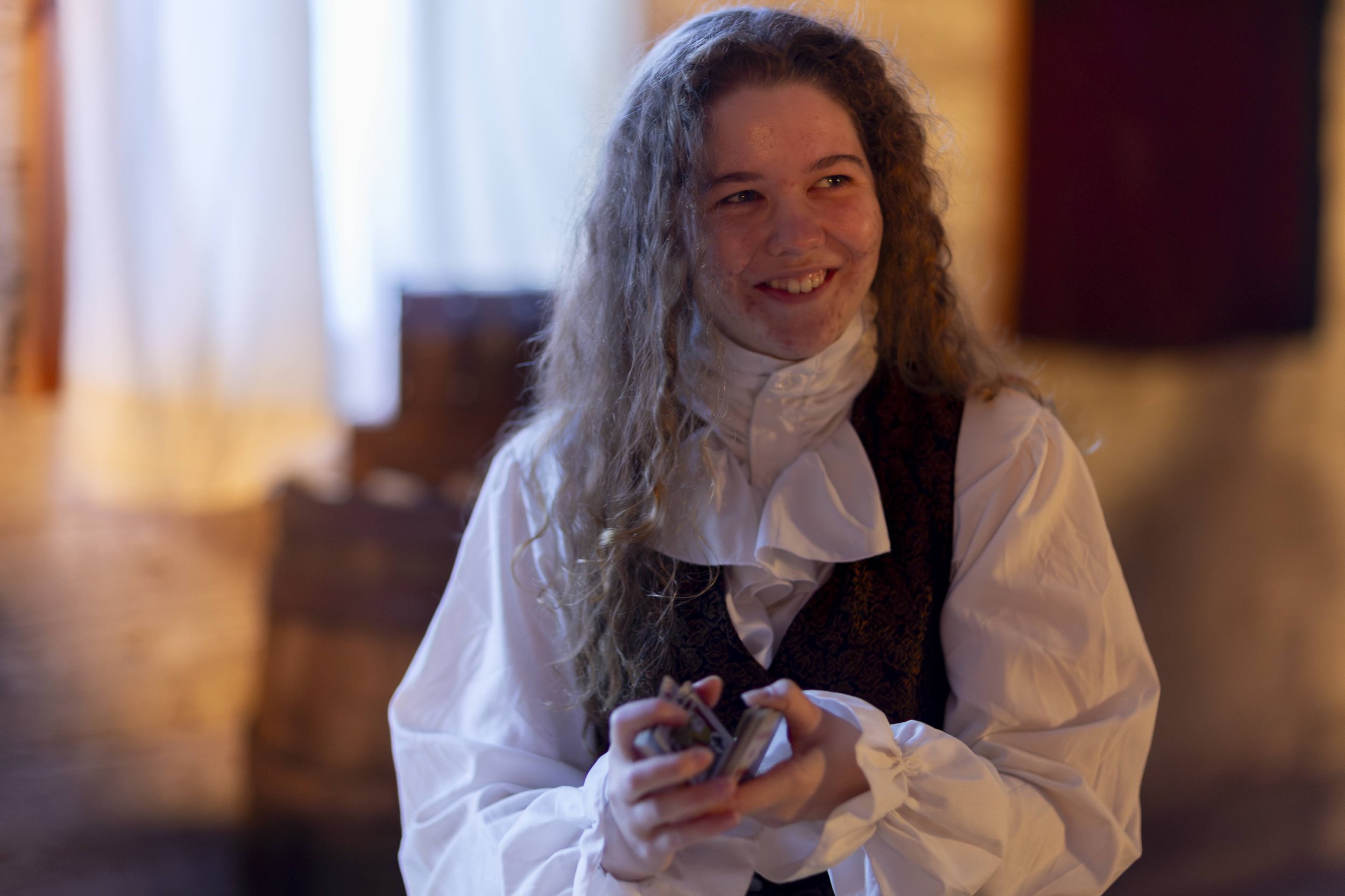 Margaret in period costume with curly hair holding playing cards