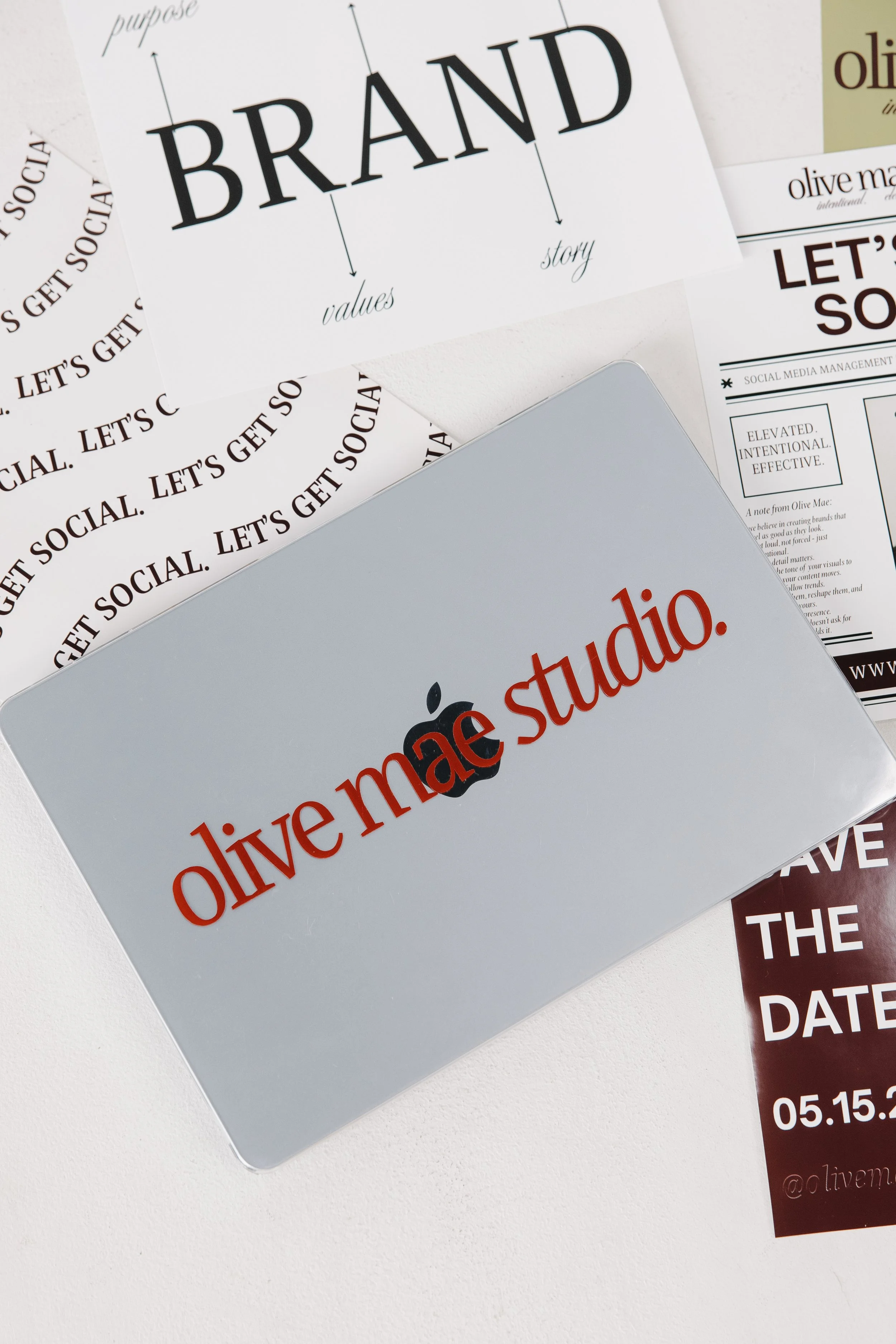 Close-up photo of various printed marketing materials on a white surface, including a card that says "olive. live your studio." in red and black text, and other promotional flyers with partially visible text related to branding and social media management.