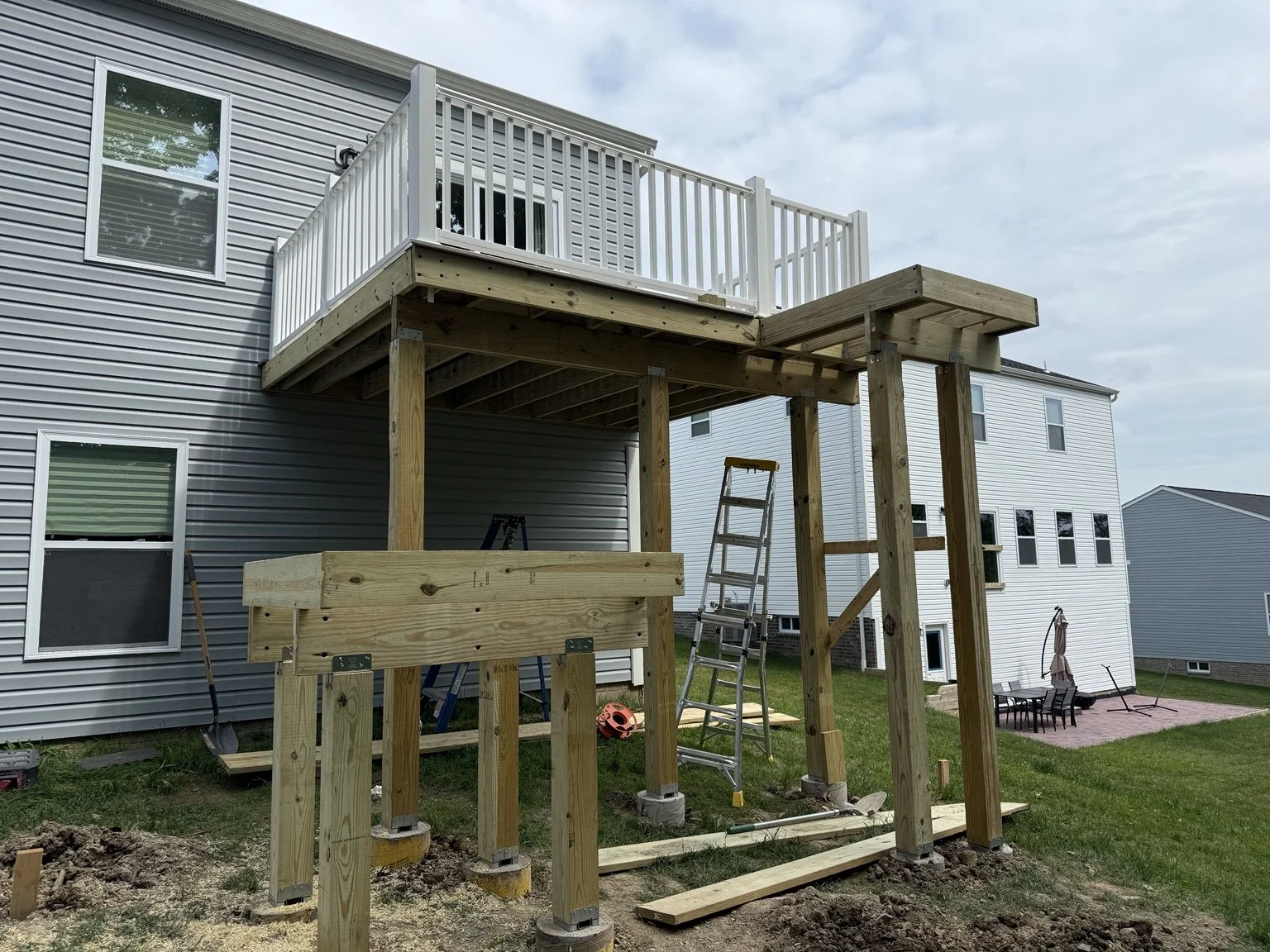 Residential deck and patio renovation project in progress in North Huntingdon, Pennsylvania. This image shows the construction of a new covered patio beneath an elevated deck, including pressure-treated structural framing and support posts prepared f