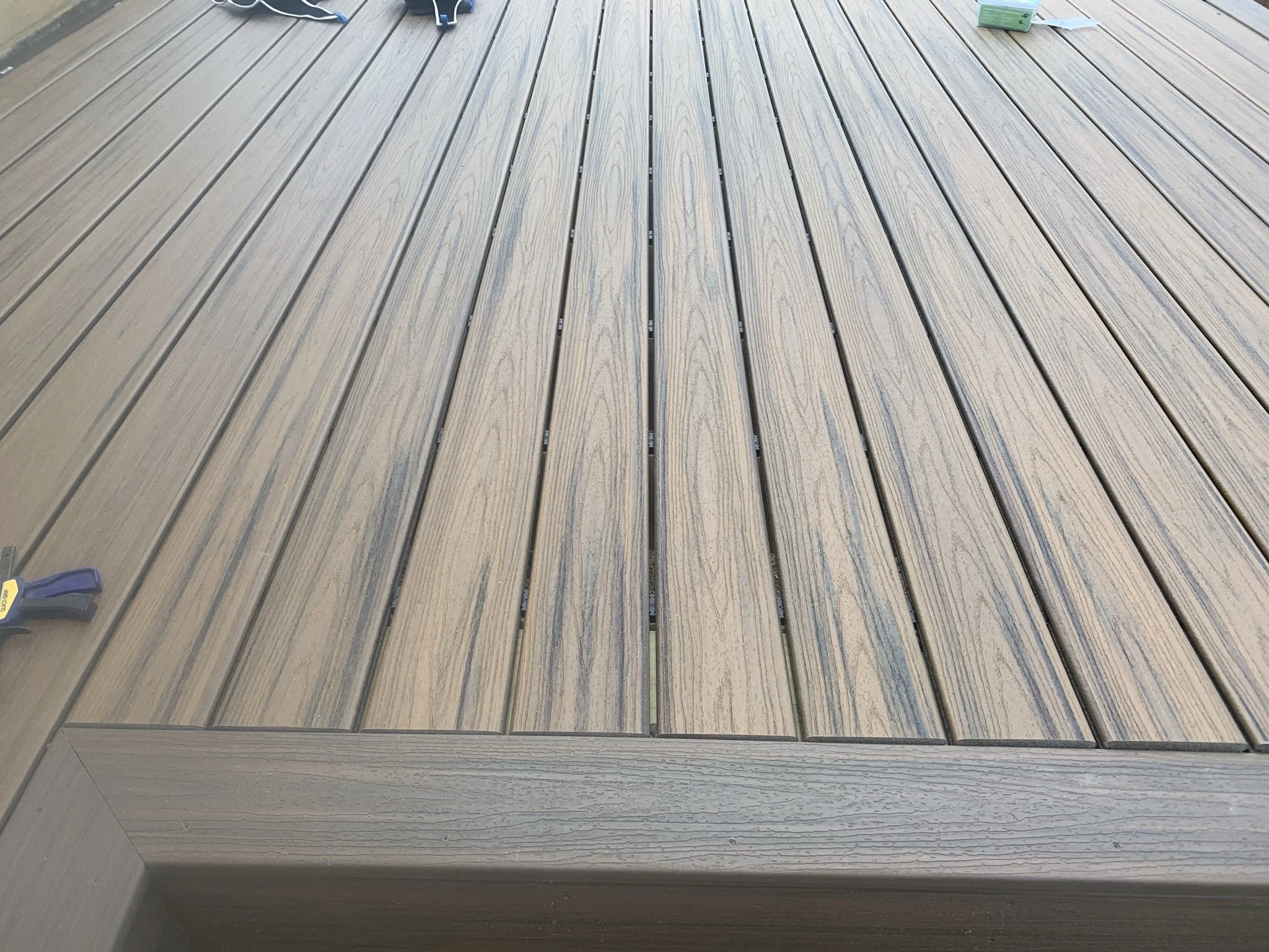 Close-up of wooden deck planks with a visible clamp on the left and some green boxes in the top right corner.