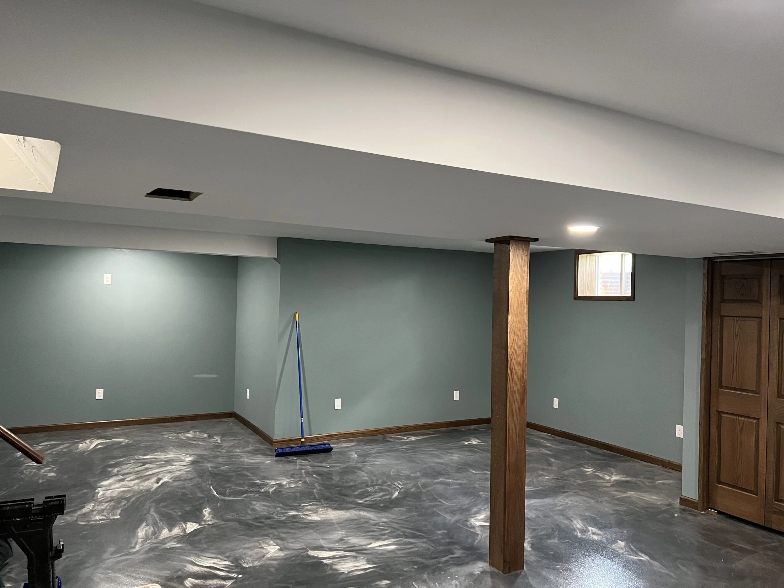Empty basement room with painted walls, a support beam, small window, and a mopped floor.