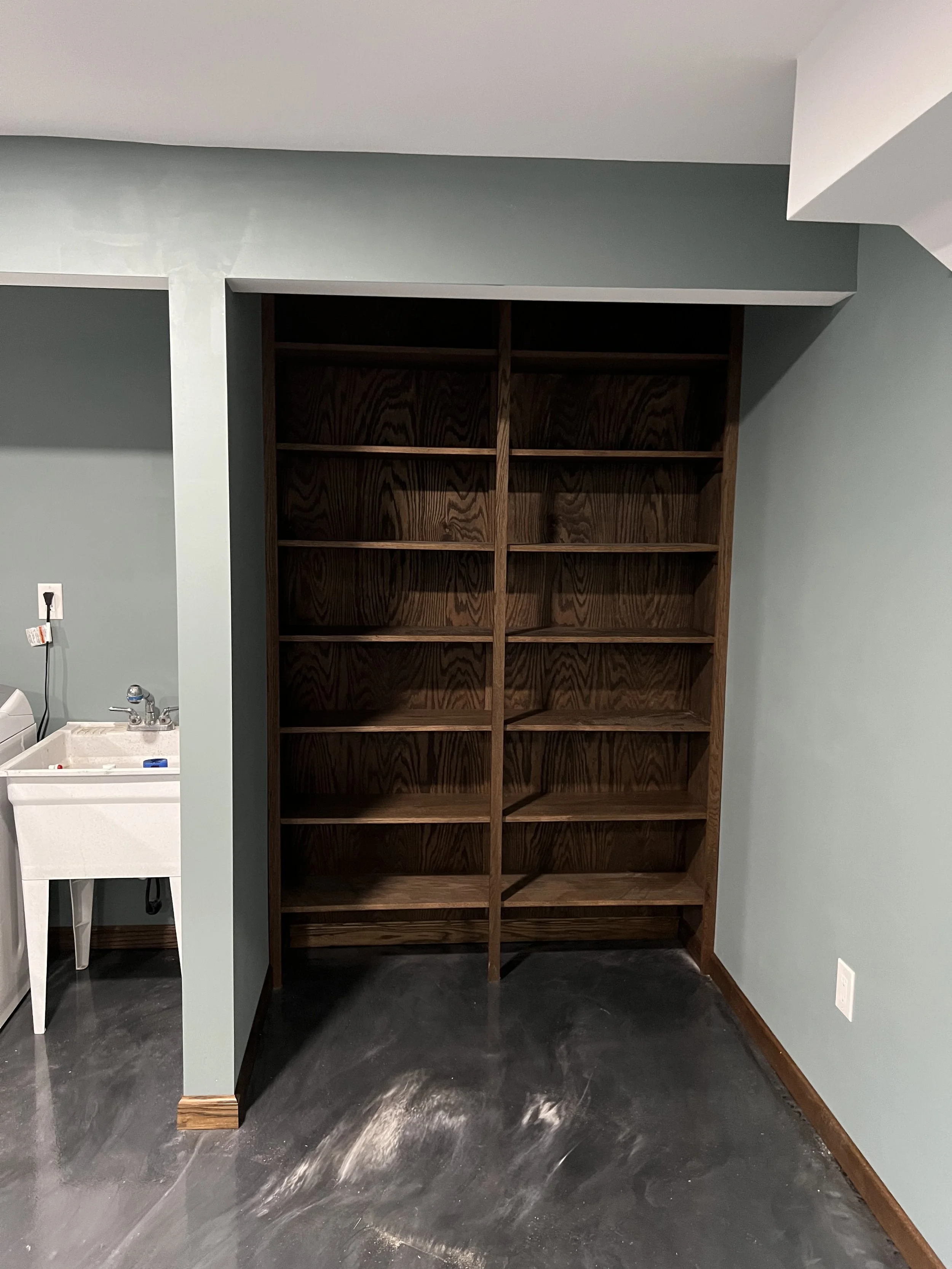 Empty wooden bookshelf with multiple shelves in a room with green walls and a concrete floor.