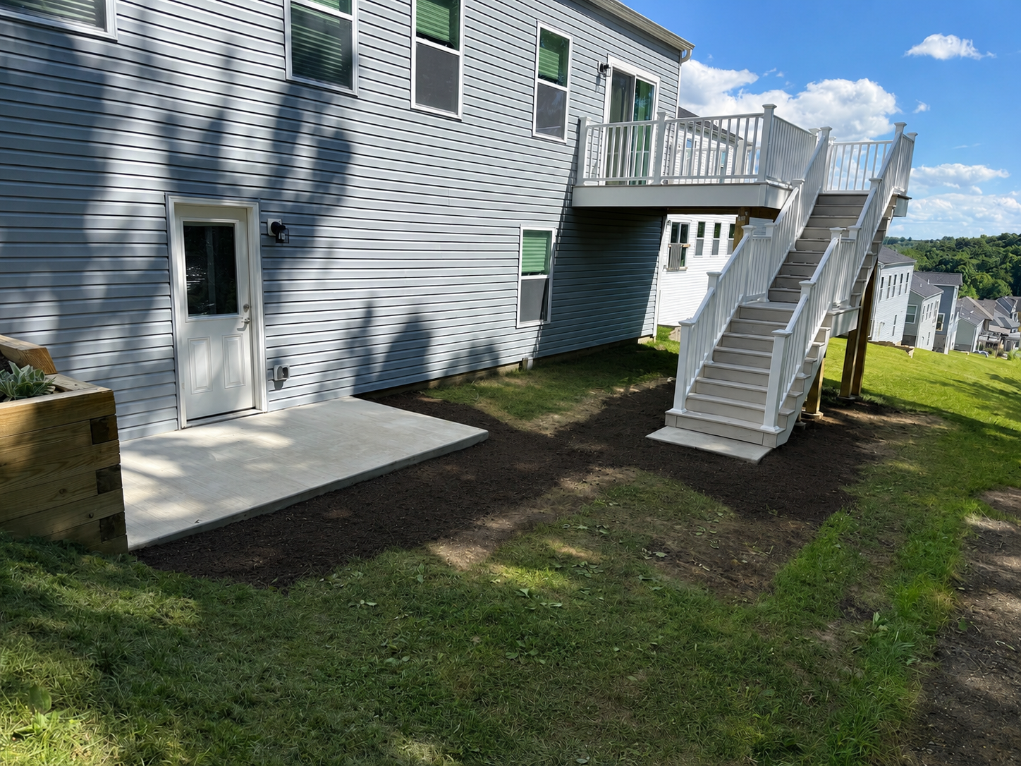 Completed residential deck and patio renovation project in North Huntingdon, Pennsylvania. This image showcases a newly constructed concrete patio, rebuilt elevated deck with a staircase, white vinyl railing, and a finished outdoor living space compl