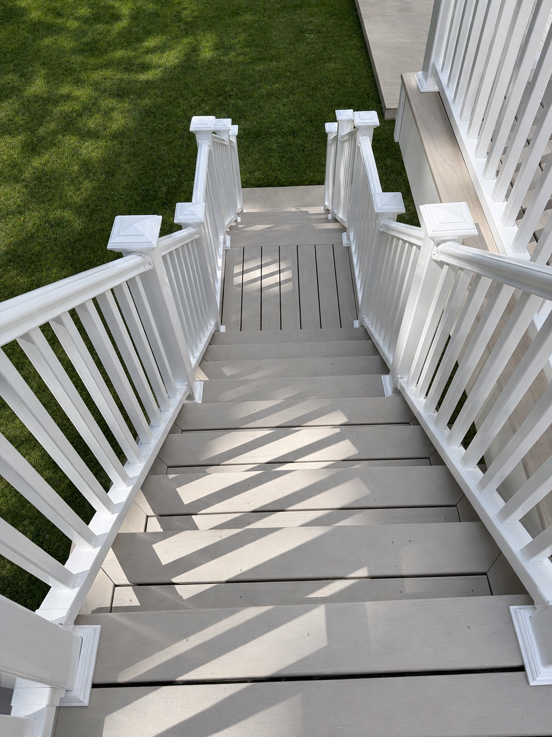 Completed residential deck and patio renovation project in North Huntingdon, Pennsylvania. This image showcases a newly constructed concrete patio, rebuilt elevated deck with a staircase, white vinyl railing, and a finished outdoor living space compl