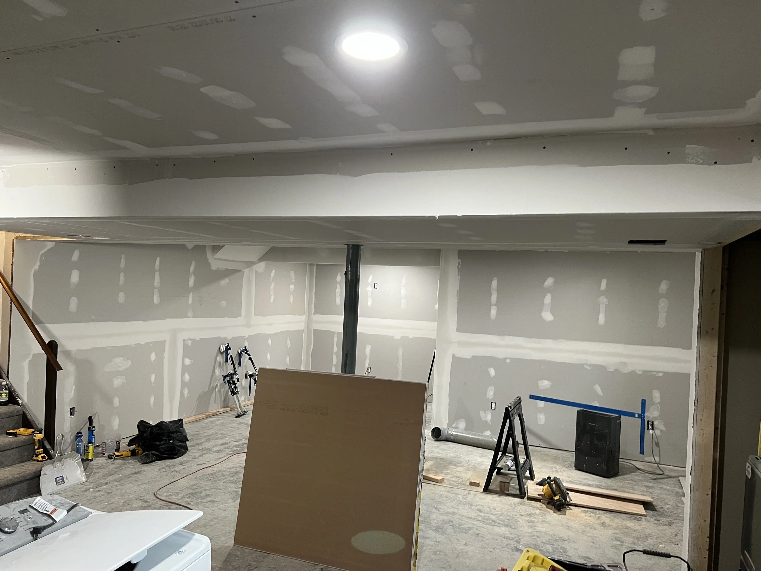 Interior room under construction with drywall walls and ceiling, tools, and construction materials scattered on the floor.