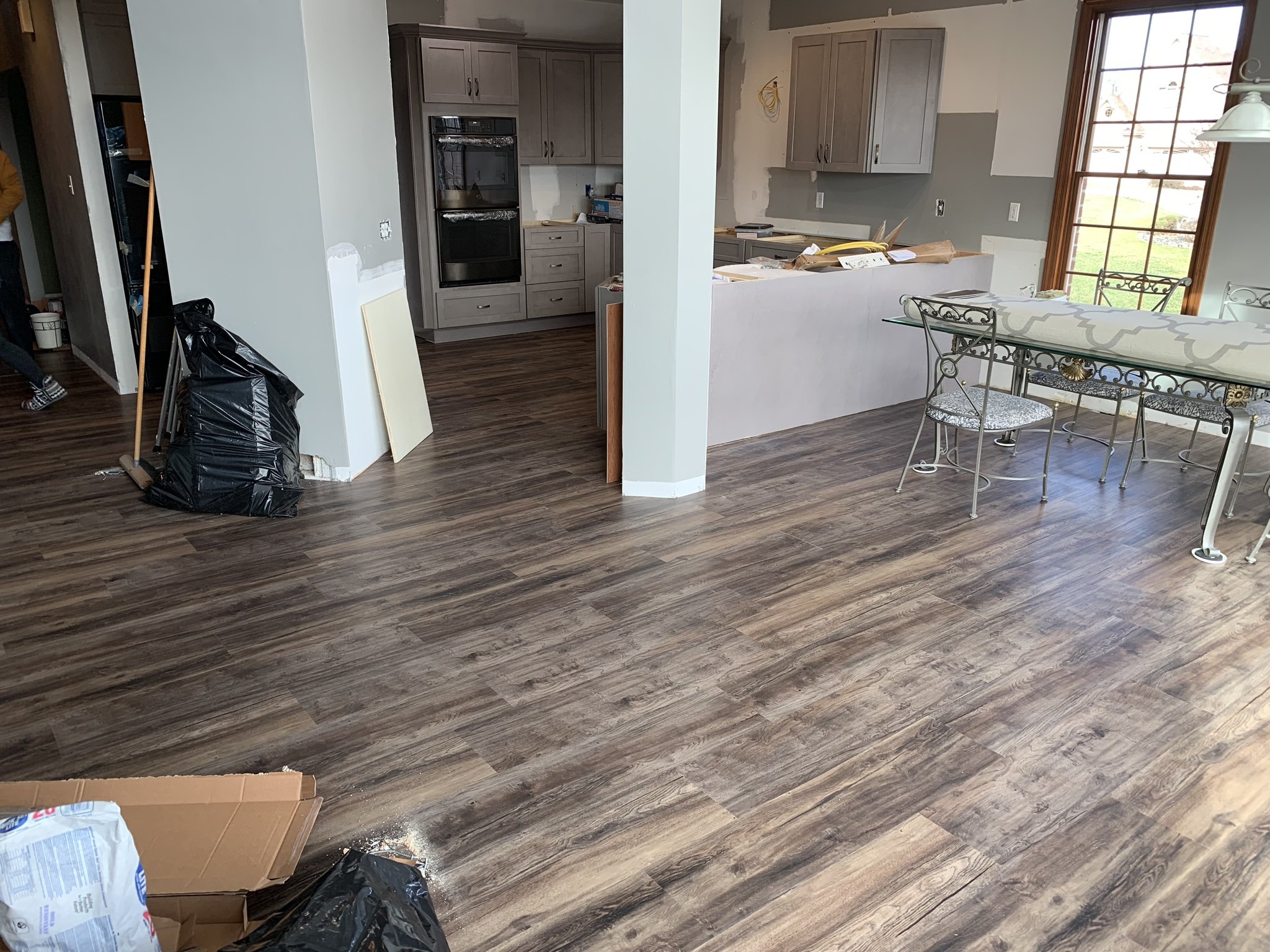 Interior of a house kitchen and dining area under renovation, with new wood-like flooring, unfinished kitchen cabinets, and construction materials.