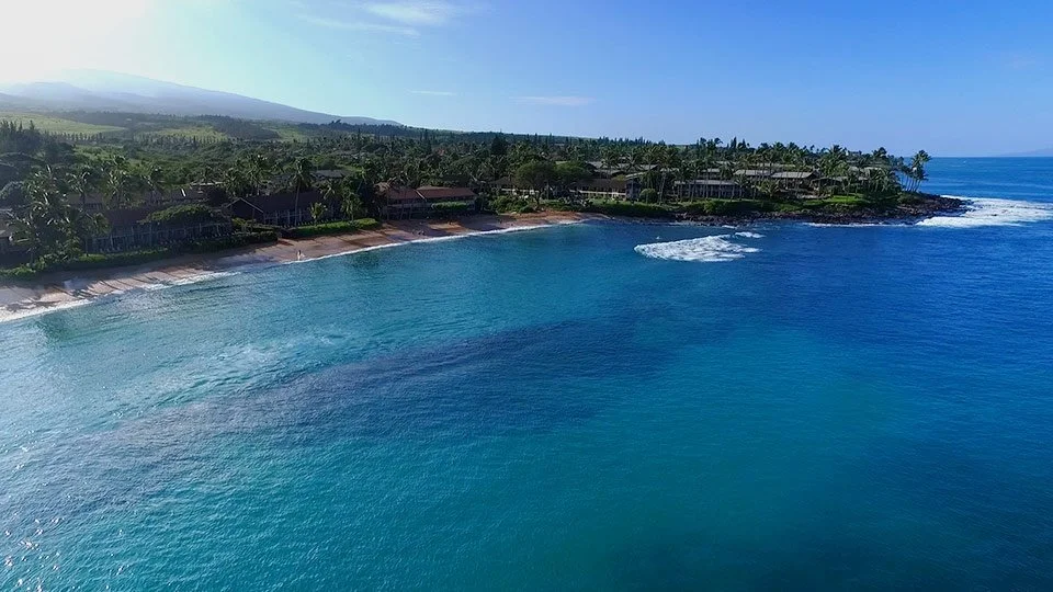 West Maui coastline showing oceanfront resorts, sunset skies, and lush hillsides