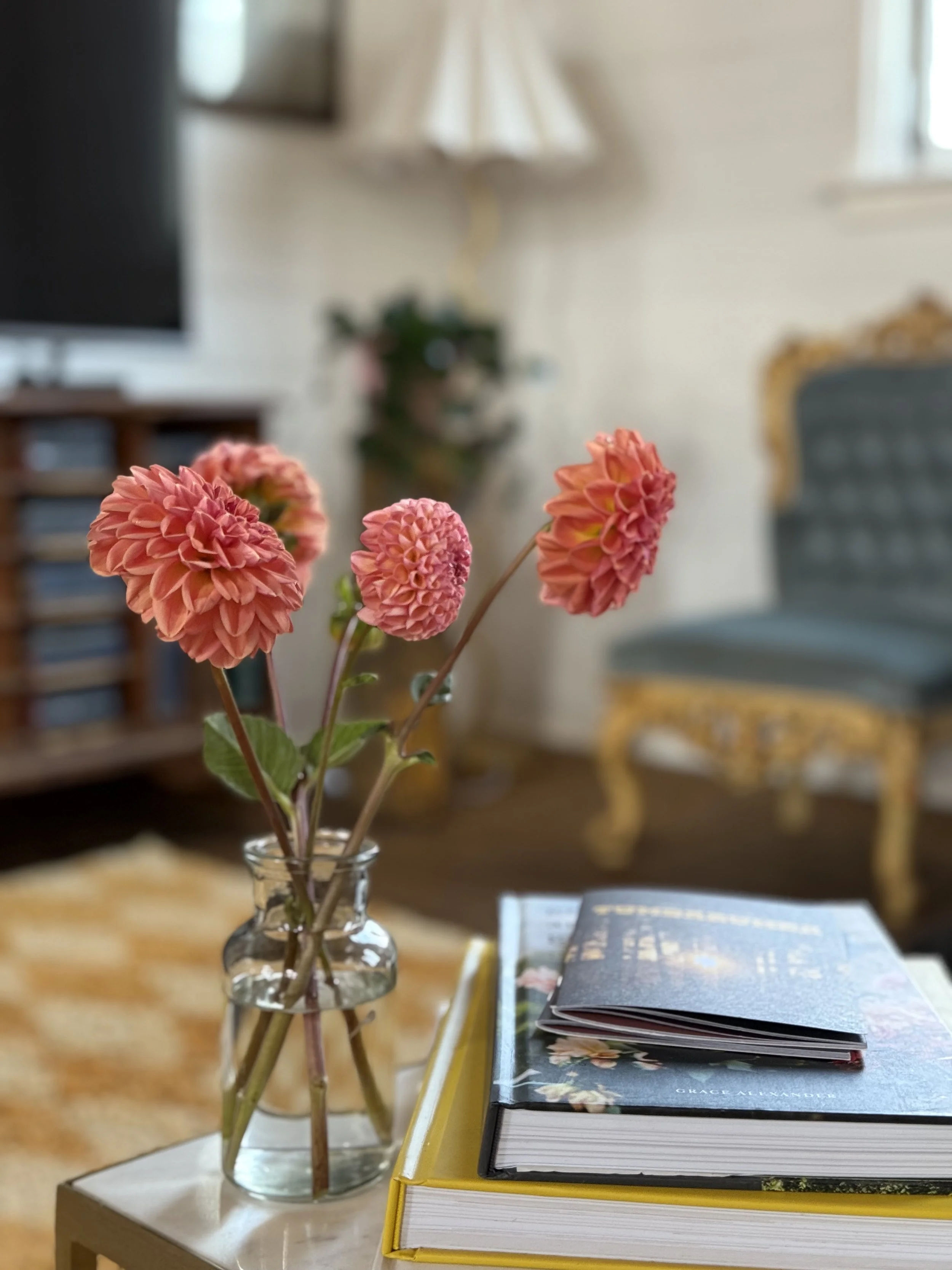 Vase with pink dahlias on a table with stacked books in a cozy living room setting.