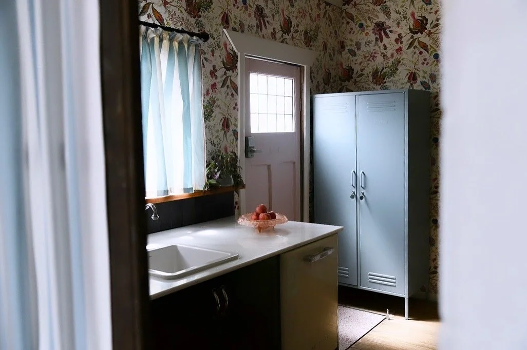 Vintage kitchen with floral wallpaper, a sink, blue cabinet, and sunlight through window and door.