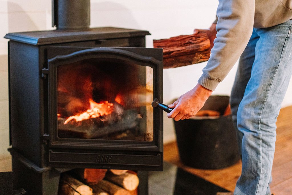 Person tending to a fire in a wood stove with a log inside.