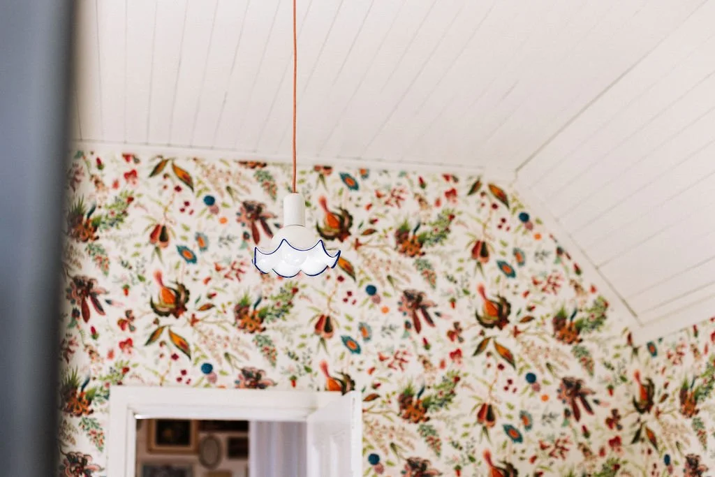 A white ceiling with a hanging cloud-shaped light fixture and floral wallpaper with red, green, and orange patterns.