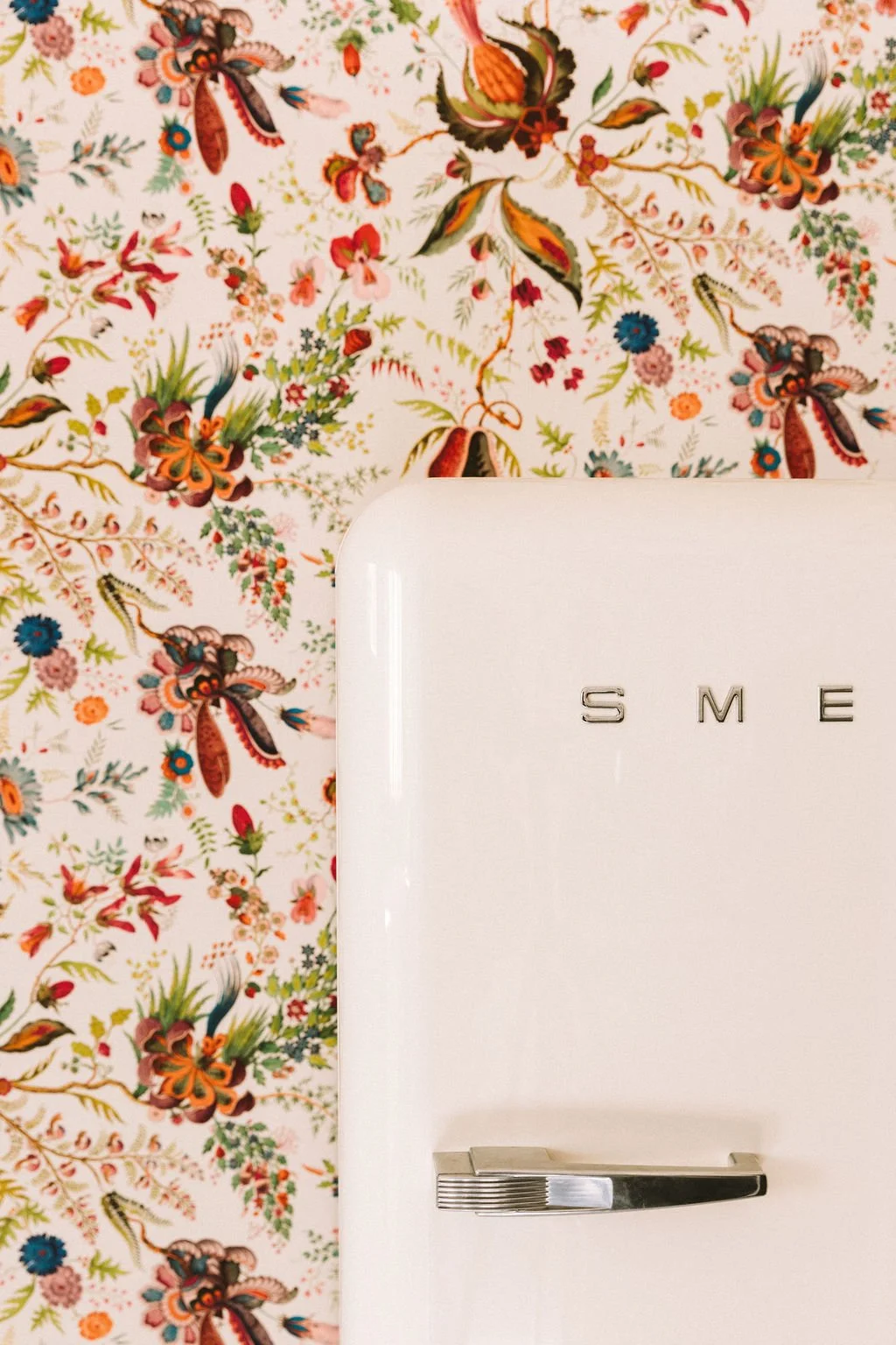 Close-up of a white SME refrigerator against a floral wallpaper background with pink, orange, green, and blue flowers and leaves.