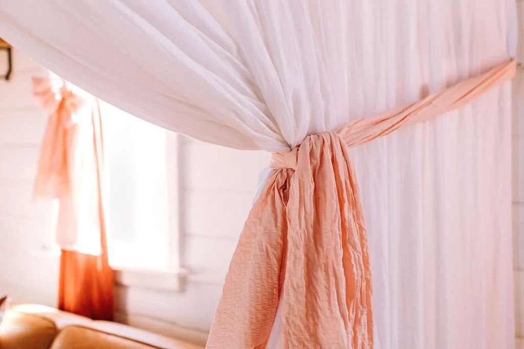 Close-up of a pink canopy bed with sheer curtains tied back with matching pink ribbons in a bright bedroom.