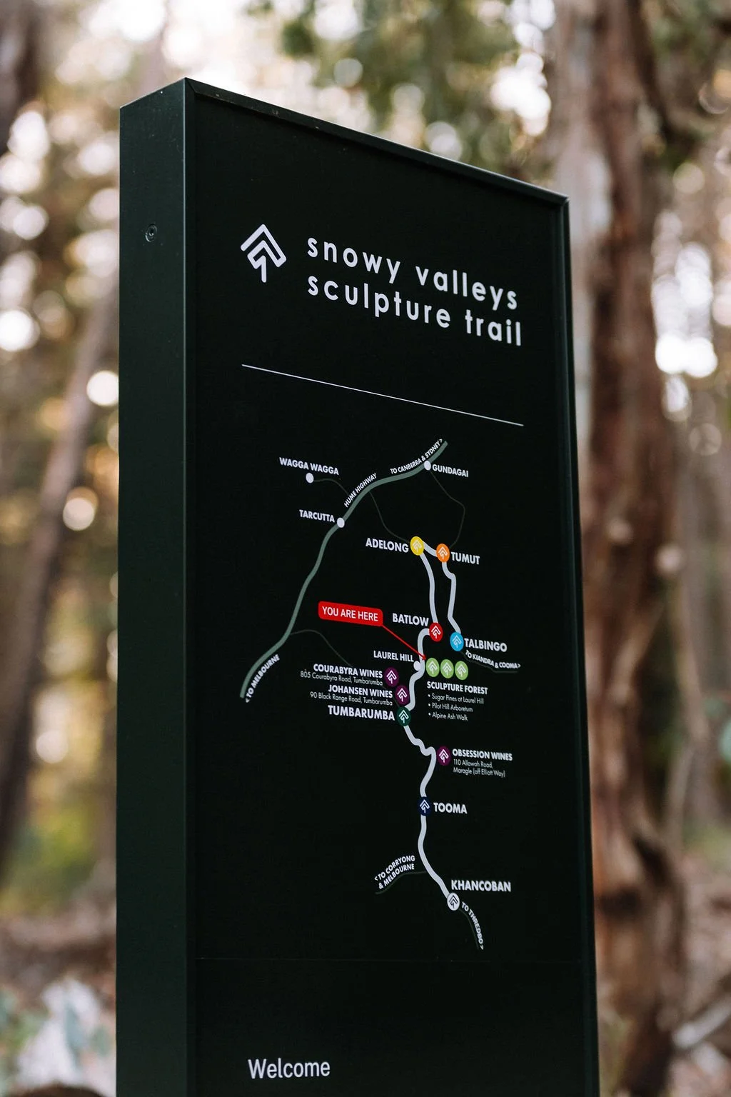 Sign for Snowy Valleys Sculpture Trail with a map showing various locations and pathways in a forest setting.