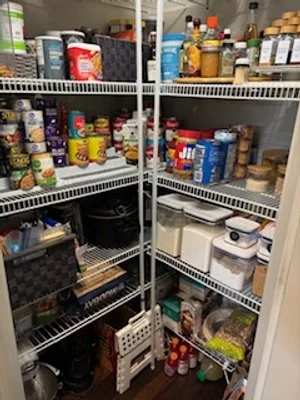 Pantry shelf filled with various canned goods, jars, and containers, including peanut butter, spices, and baking ingredients.