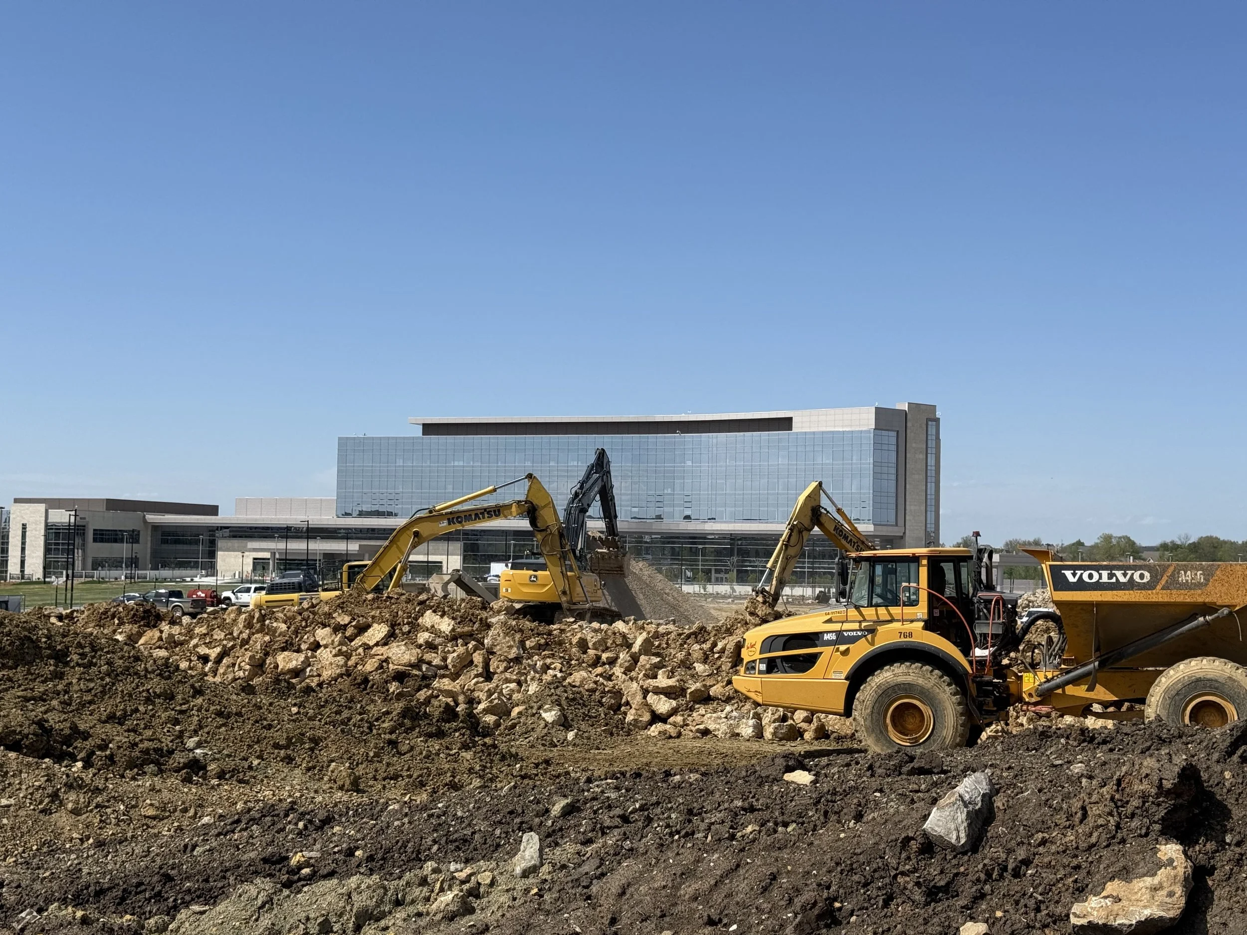 Construction site with excavators and a large modern building in the background.