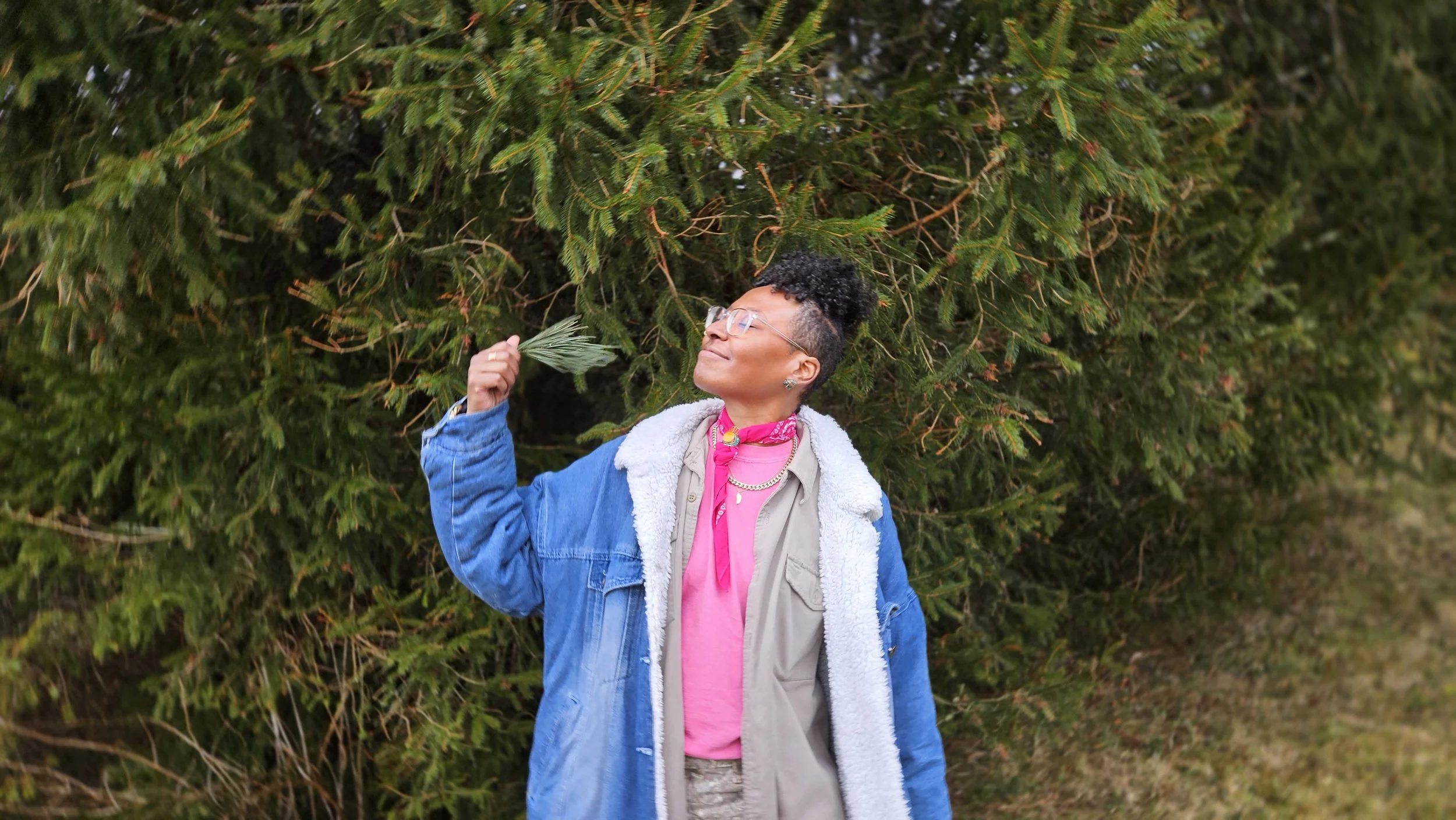 Black human in front of conifer trees waving bundle of pine needles