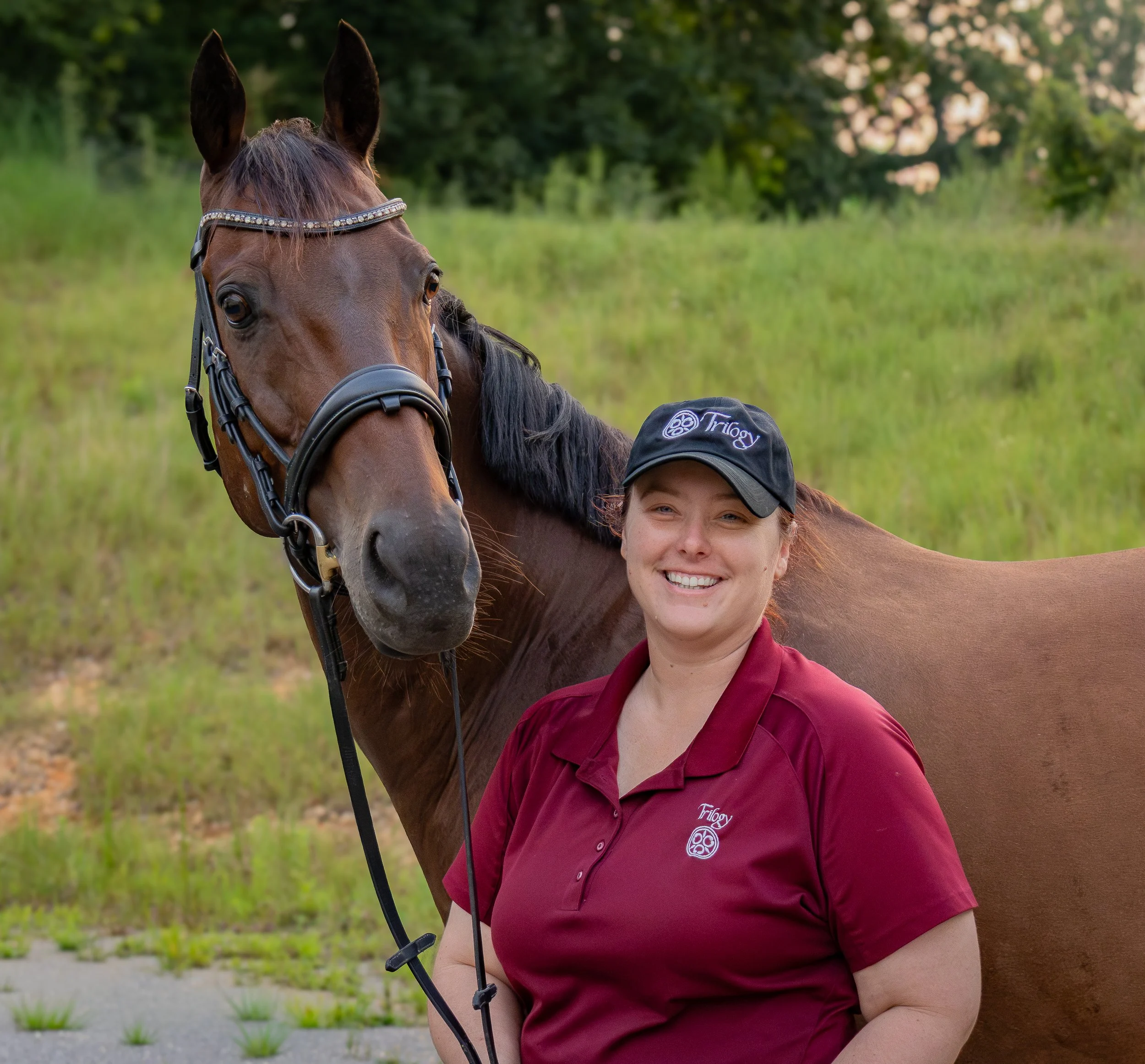 A saddle fitter in a maroon polo shirt and a black baseball cap standing next to a brown horse